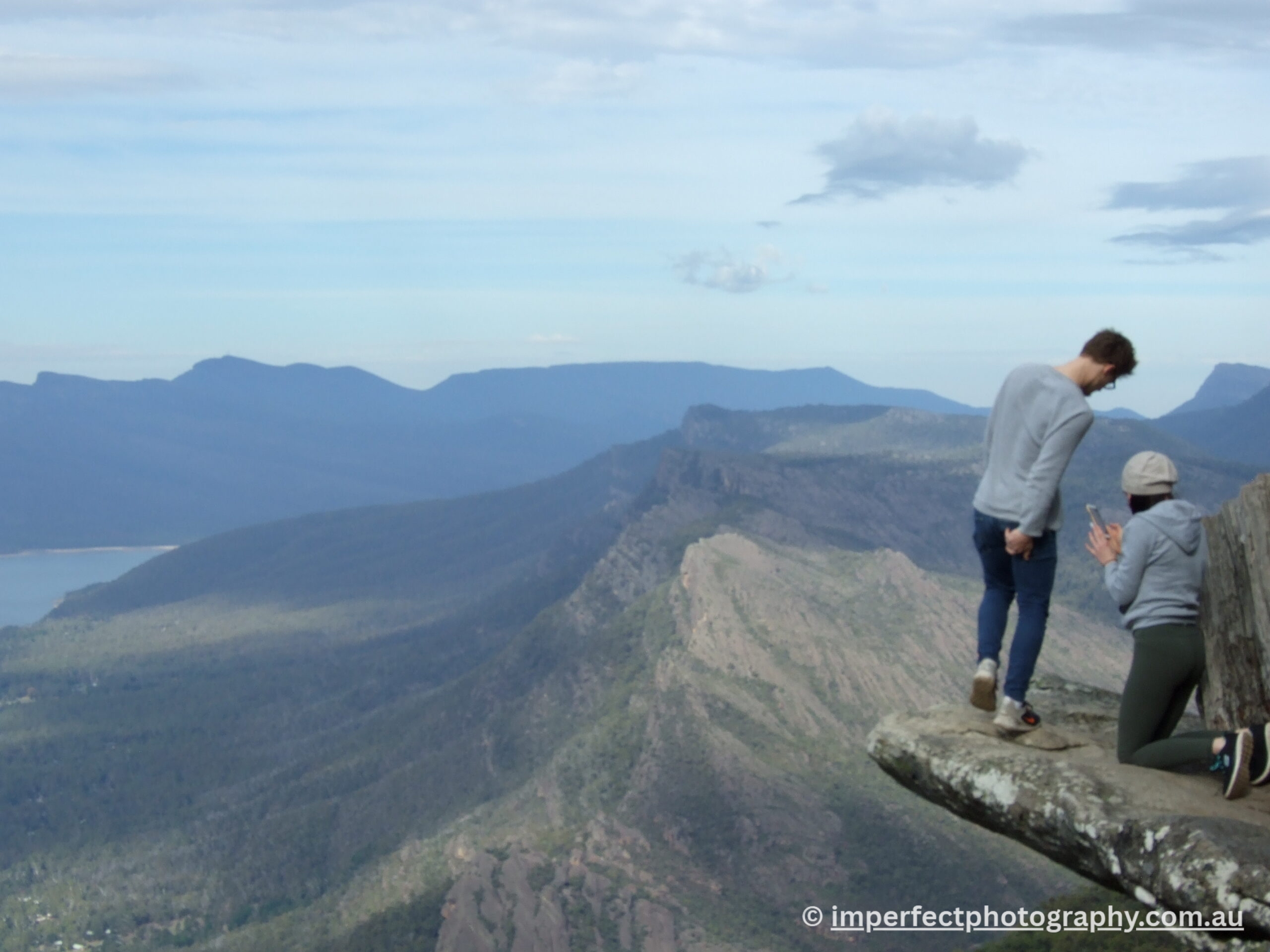 Mountains with blue sky and two people on a rock cliff